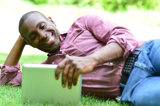 Relaxed man lying on the lawn, watching his tablet