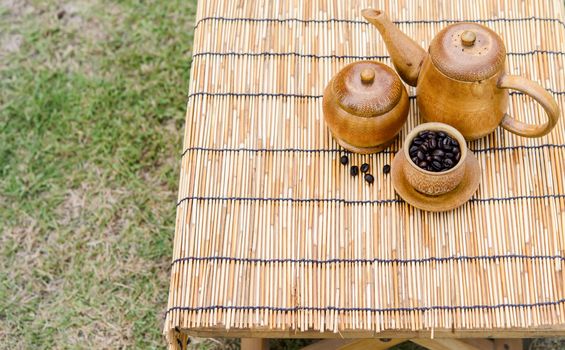 Coffee beans, cup of coffee and teapot on bamboo wooden desk. Set of cafe