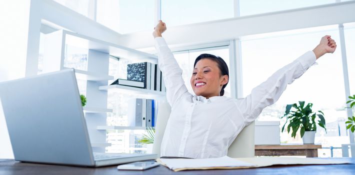 Businesswoman cheering behind laptop computer in office