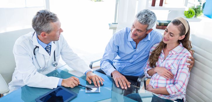 Pregnant woman and her husband discussing with doctor in clinic