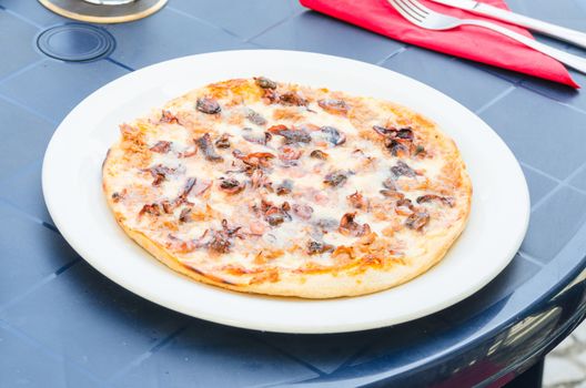 Pizza with seafood on a simple blue table in a garden restaurant.