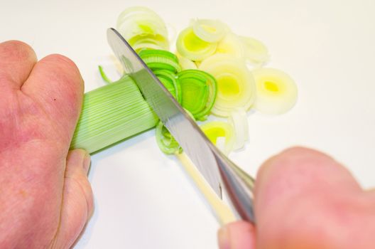 Hand of the cook, while cutting vegetables on a wooden board.
