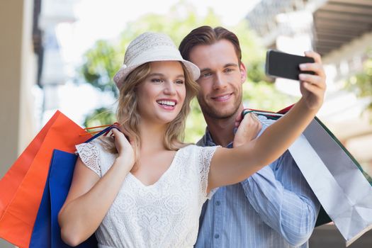 Cute couple taking a selfie while holding shopping bags 