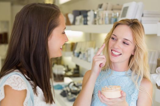 Happy blonde woman applying cosmetic products in a beauty salon