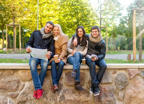 travel, vacation, people, tourism and friendship concept - group of smiling friends sitting with tablet pc computer map and hot drinks in park