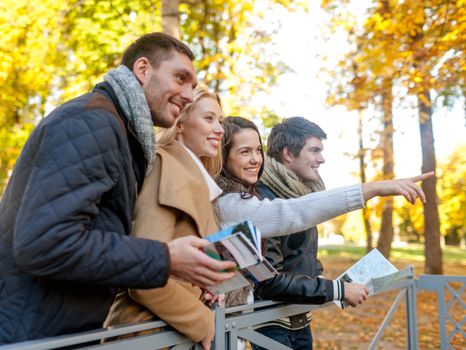 travel, people, tourism, gesture and friendship concept - group of smiling friends with map standing on bridge and pointing finger in city park