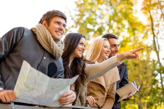 travel, people, tourism, gesture and friendship concept - group of smiling friends with map standing on bridge and pointing finger in city park