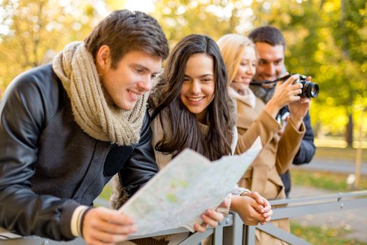 travel, vacation, technology, tourism and friendship concept - group of smiling friends with digital photo camera and map in city park