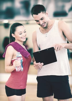 fitness, sport, training, gym and lifestyle concept - smiling male trainer with clipboard and woman with water bottle in the gym