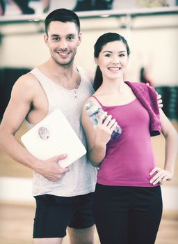 fitness, sport, training, gym and lifestyle concept - two smiling people with scale and water bottle in the gym