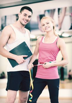fitness, sport, training, diet and lifestyle concept - two smiling people with clipboard and measure tape in the gym