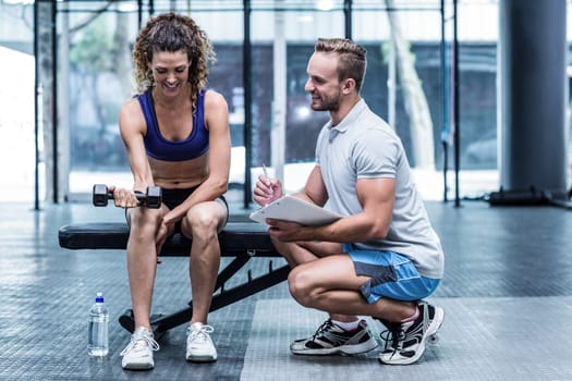 Trainer supervising a muscular woman lifting a dumbbell