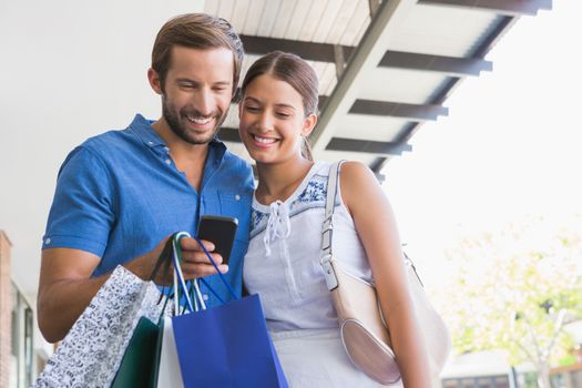 Young happy couple looking at mobile phone after shopping