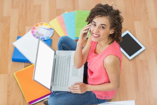 Young creative businesswoman working on laptop while on the phone