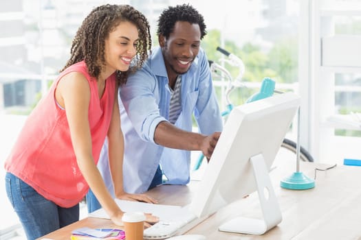 Two smiling creative business colleagues discussing over a computer