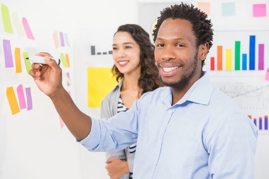 Young smiling creative business people writing at sticky notes and facing to the camera