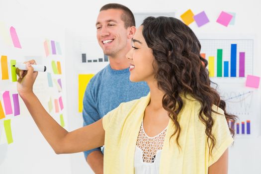 Smiling coworkers writing on sticky notes in the office