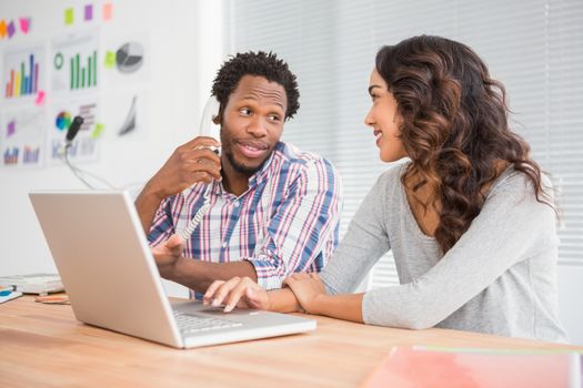 Young business people on the laptop and telephone smiling at each other