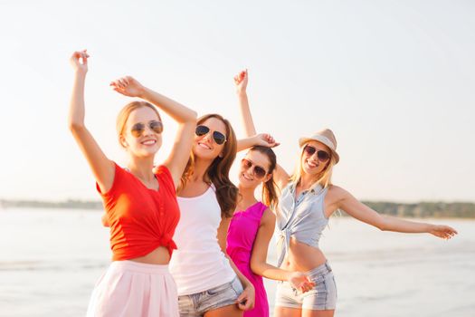 summer vacation, holidays, travel and people concept - group of smiling young women in sunglasses and casual clothes dancing on beach