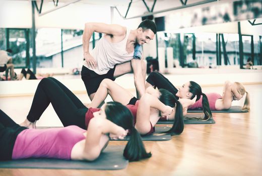 fitness, sport, training, gym and lifestyle concept - group of smiling women with male trainer doing sit ups on mats in the gym