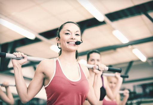 fitness, sport, training, gym and lifestyle concept - smiling trainer in front of the group of people working out with barbells in the gym