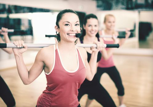 fitness, sport, training, gym and lifestyle concept - smiling trainer in front of the group of people working out with barbells in the gym