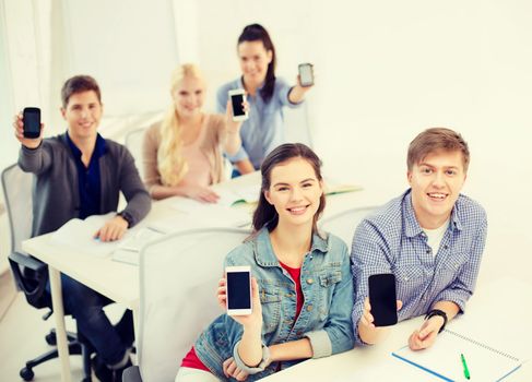 education, school, technology and internet concept - smiling students showing black blank smartphone screens at school