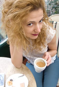 young blonde woman drinking coffee sitting on the chair with prone and cookie on the table