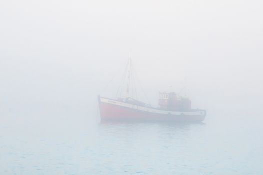 LUDERITZ, NAMIBIA - JUNE 13, 2011: A fishing boat is barely visible through thick mist at the harbor in Luderitz