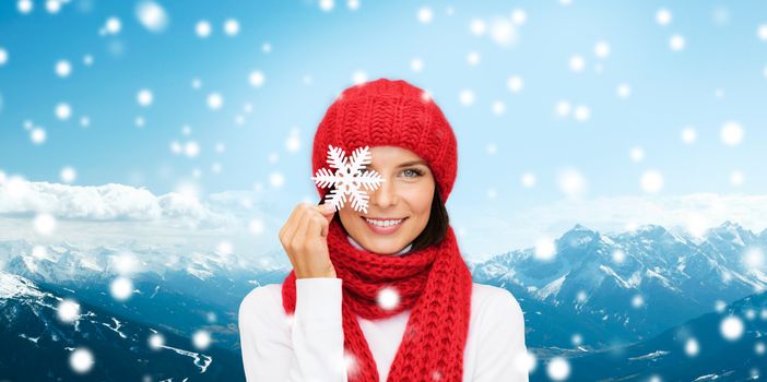 happiness, winter holidays, tourism, travel and people concept - smiling young woman in red hat and mittens holding snowflake over snowy mountains background