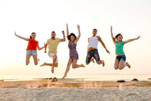 friendship, summer vacation, holidays, party and people concept - group of smiling friends dancing and jumping on beach