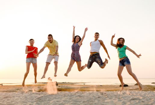 friendship, summer vacation, holidays, party and people concept - group of smiling friends dancing and jumping on beach