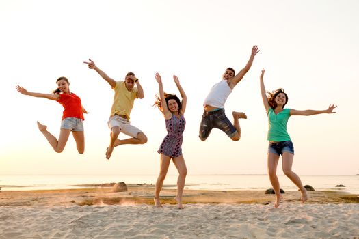 friendship, summer vacation, holidays, party and people concept - group of smiling friends dancing and jumping on beach