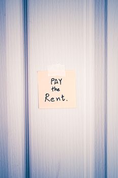 sticky note write a message pay the rent on wood door background vintage style