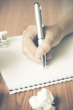 woman hand writing with pen on notebook.there are crumpled paper and coffee cup on wood table background vintage style