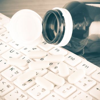 pills on keyboard computer on wooden background concept technology addiction vintage style