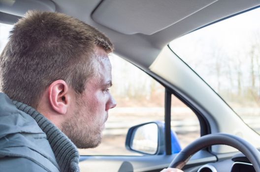 Young man driving a car, holding his right hand on the steering wheel.