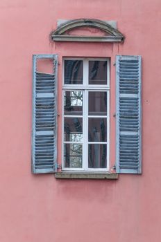 An old window with blue shutters opened at an old house. Red facade.