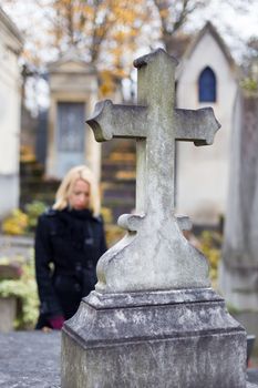 Solitary woman mourning by gravestone, remembering dead relatives in on Pere Lachaise cemetery in Paris, France.