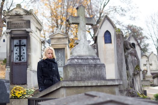 Solitary woman mourning by gravestone, remembering dead relatives in on Pere Lachaise cemetery in Paris, France.