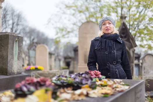 Solitary woman mourning by gravestone, remembering dead relatives in on Pere Lachaise cemetery in Paris, France.