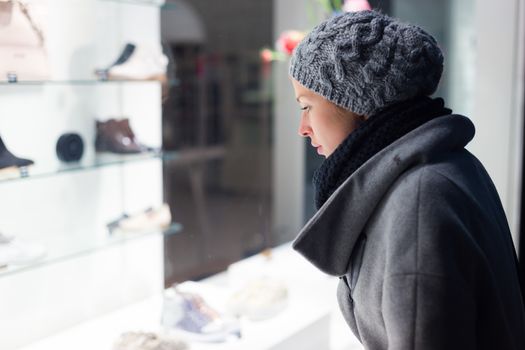 Casualy winter dressed lady window shopping in front of sinfully expensive boutique store dispaly window. Customer woman in shopping street, looking at window, outdoor.