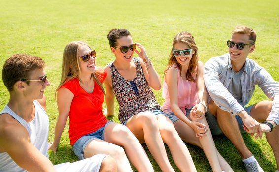 friendship, leisure, summer and people concept - group of smiling friends outdoors sitting and talking on grass on grass in park