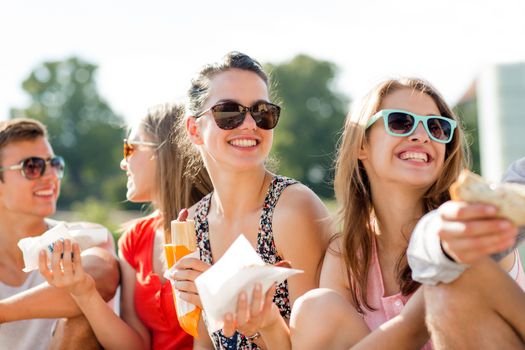 friendship, leisure, summer and people concept - group of smiling friends in sunglasses sitting with food on city square