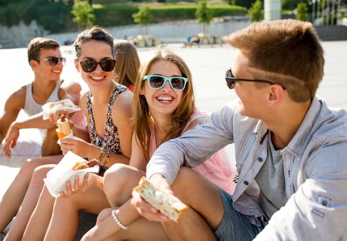 friendship, leisure, summer and people concept - group of smiling friends in sunglasses sitting with food on city square