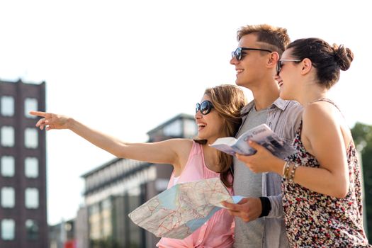 travel, tourism, vacation, summer and people concept - smiling friends with map and city guide pointing finger outdoors