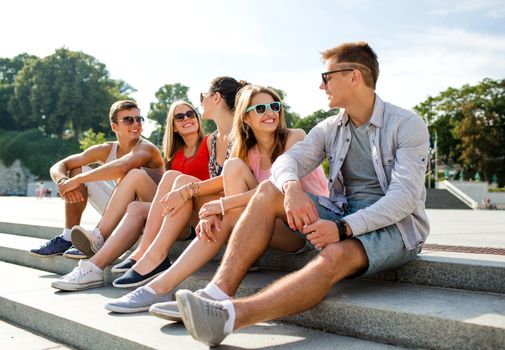 friendship, leisure, summer and people concept - group of smiling friends sitting on city street