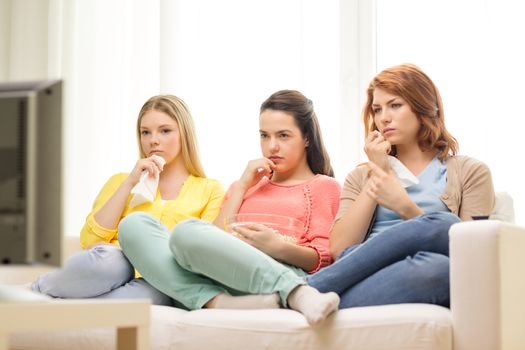 home, technology and friendship concept - three sad teenage girl watching tv at home and eating popcorn