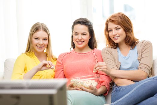 home, technology and friendship concept - three smiling teenage girl watching tv at home and eating popcorn