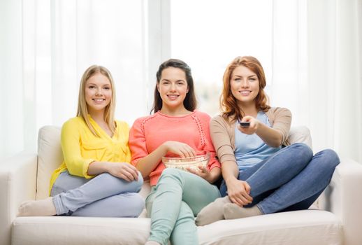 home, technology and friendship concept - three smiling teenage girl watching tv at home and eating popcorn